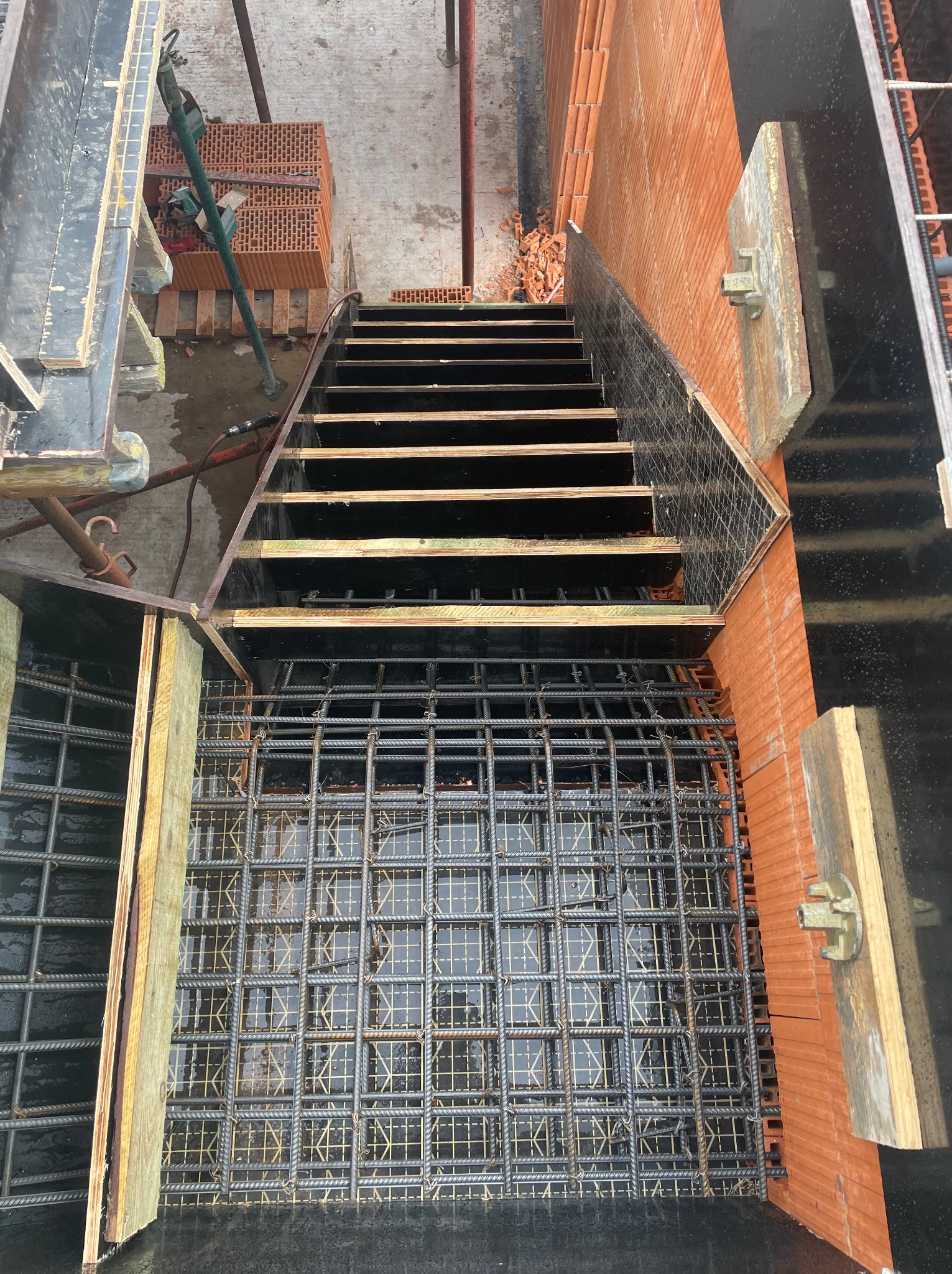 Zbrojenie fundamentu z widoczną konstrukcją schodów i cegłą klinkierową. Widok z góry na plac budowy.