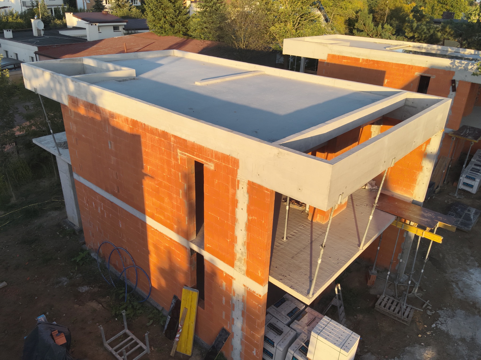 Budowa domu w stanie surowym otwartym z pomarańczowych bloczków, widoczne zbrojenia i szalunki. Ujęcie z góry w słoneczny dzień.