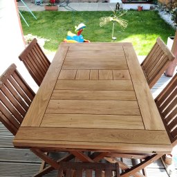 Drewno - Drewniany stół ogrodowy z krzesłami na tarasie z desek kompozytowych, w tle trawnik i dom z cegły.