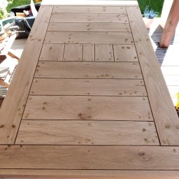 Drewno - Detal drewnianego tarasu w trakcie budowy: widoczne deski z otworami po wkrętach, narzędzia w torbie obok, zabawka dziecięca w tle.