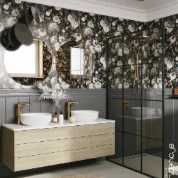 Elegancka łazienka z ciemną tapetą w kwiaty, okrągłymi lustrami i złotą armaturą, kabina prysznicowa z czarnymi ramami, drewniana szafka pod umywalką.