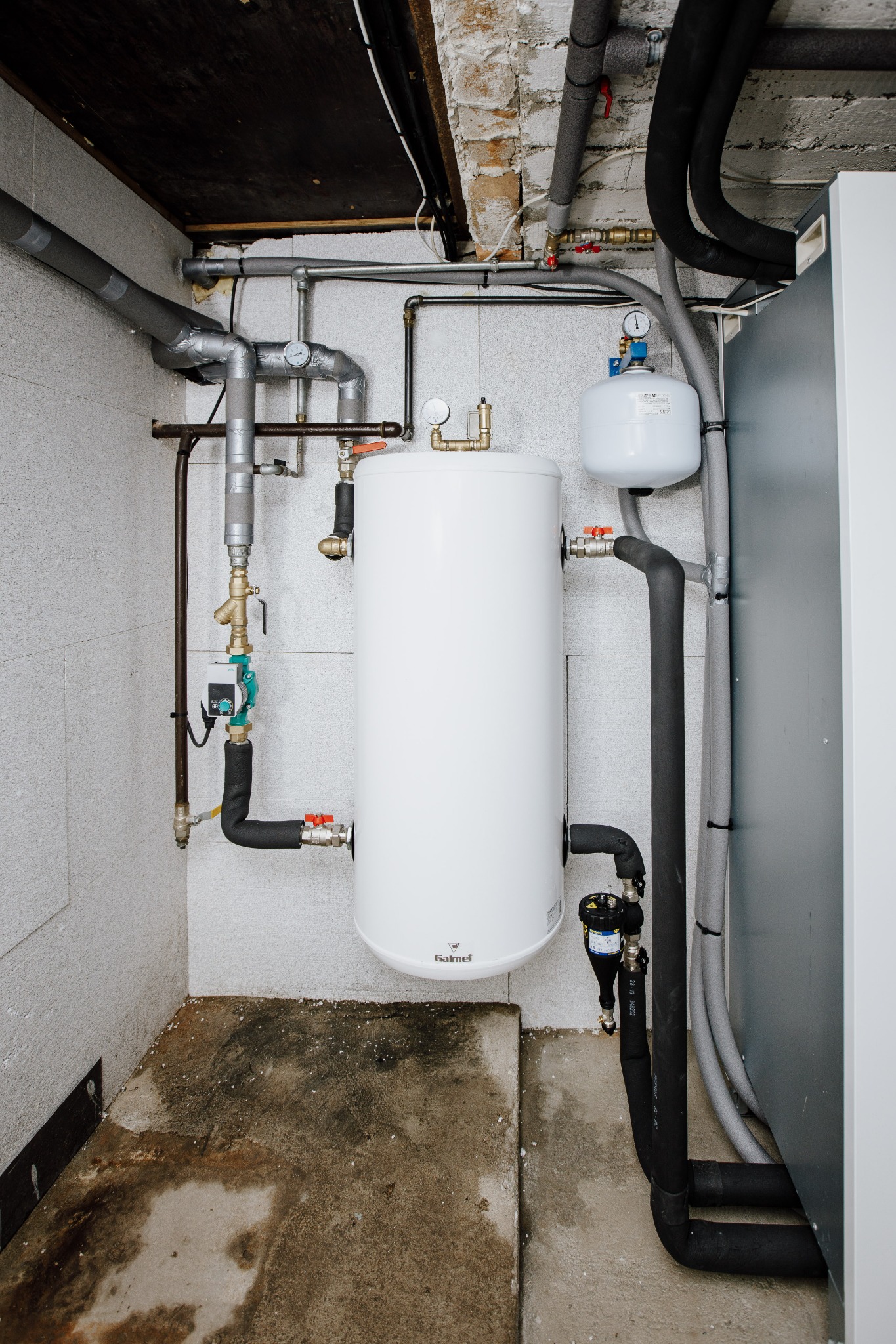 Biały zbiornik buforowy Galmet z orurowaniem, zaworami i manometrami w kotłowni z betonową podłogą i instalacjami pod sufitem.