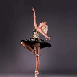 Profesjonalne studyjne zdjęcie baleriny w czarno-złotej sukience, stojącej na pointach na szarym tle.
