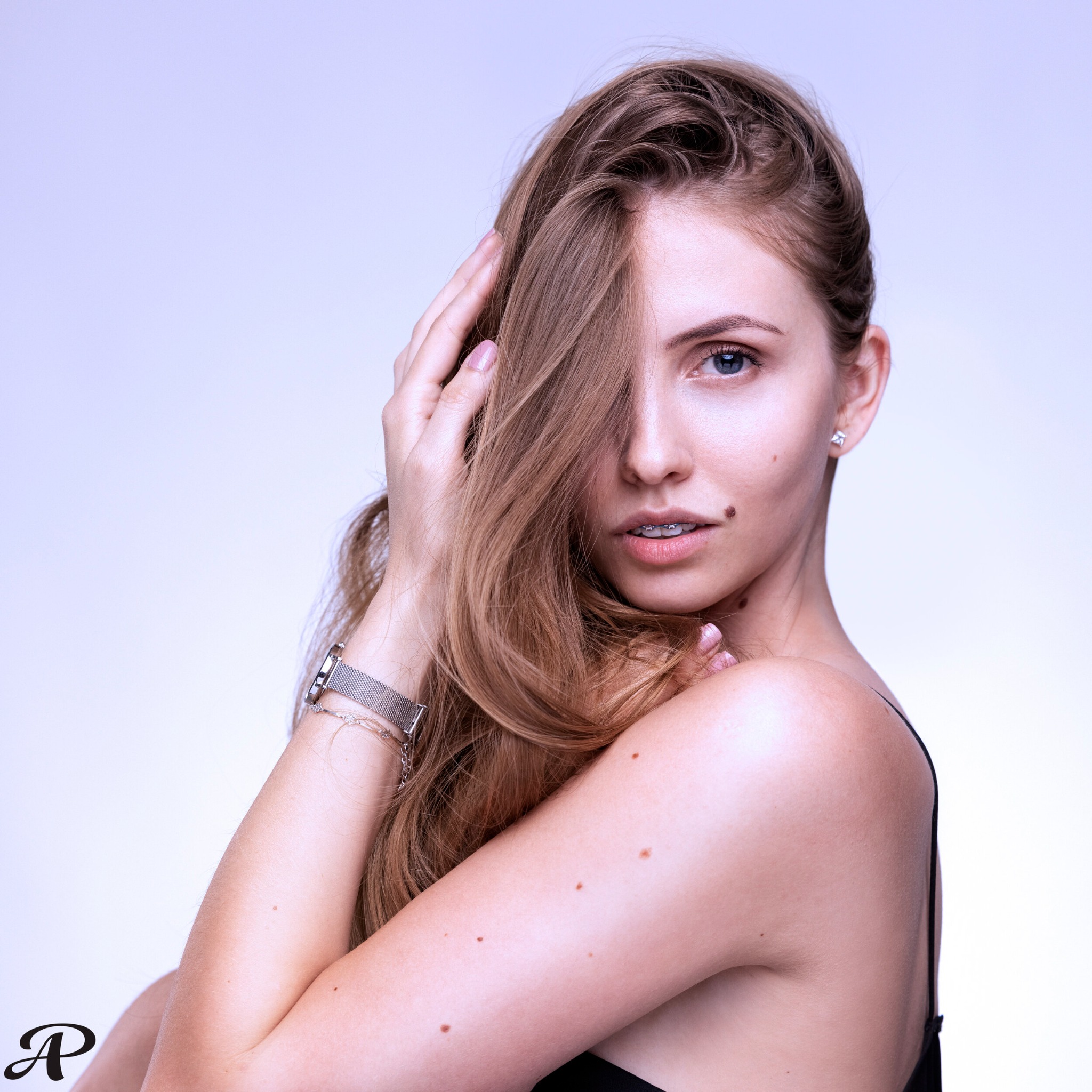 Portret młodej kobiety z blond włosami, z aparatem ortodontycznym na zębach, pozującej na jasnym tle.