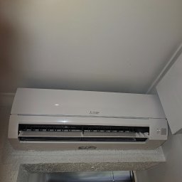 EKOTERM Andrzej Białoszewski - Biała jednostka wewnętrzna klimatyzacji Mitsubishi Electric zamontowana nad przejściem w pomieszczeniu z teksturowaną ścianą.