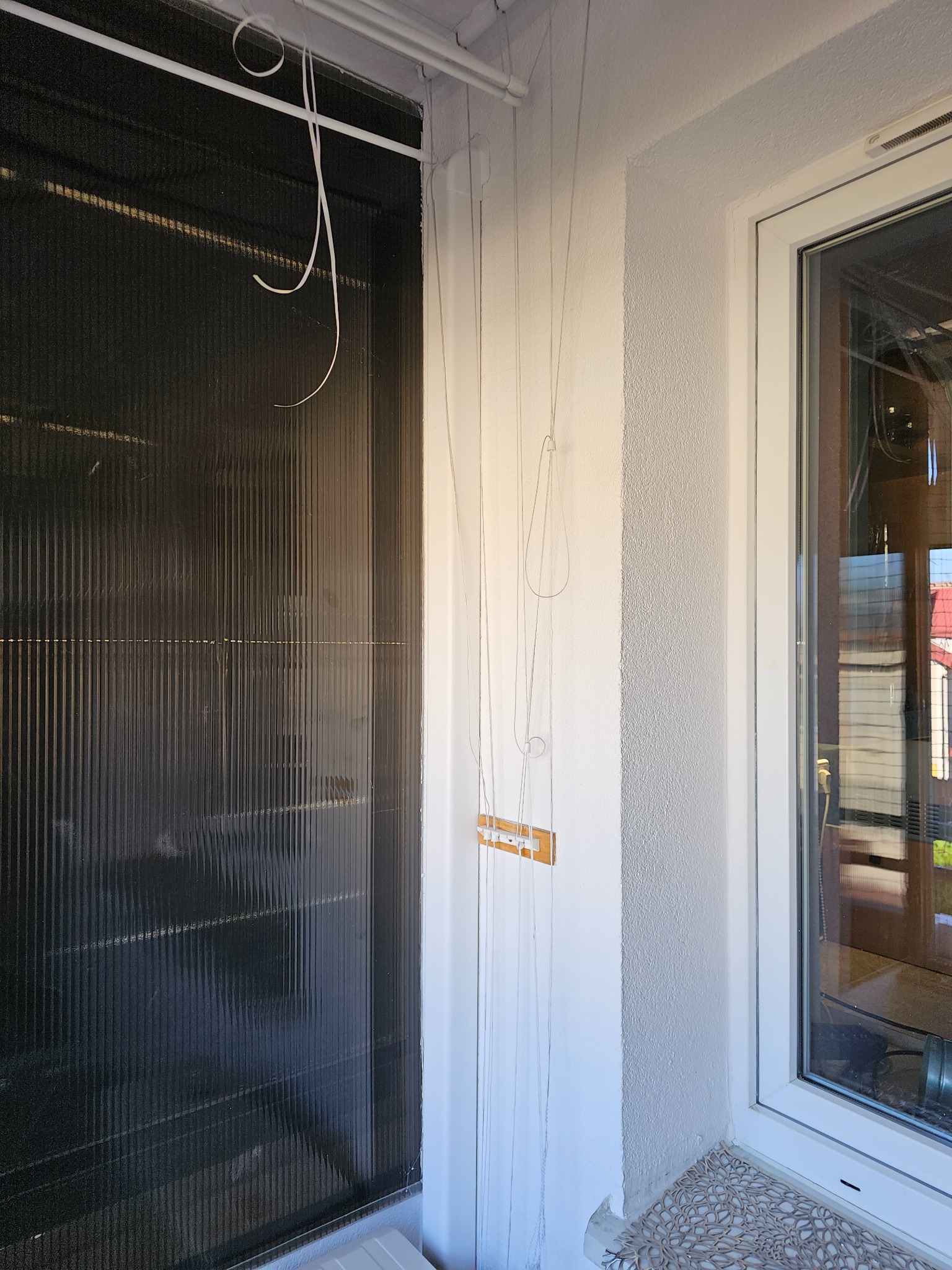 Ciemny kolektor słoneczny z wiszącymi przewodami montażowymi w trakcie instalacji wewnątrz pomieszczenia, widok z boku okna.