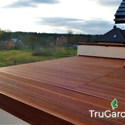 Trugarden Krzysztof Truszewski - Kompozytowy taras na dachu domu z widokiem na wiejską okolicę, logo TruGarden w prawym dolnym rogu.