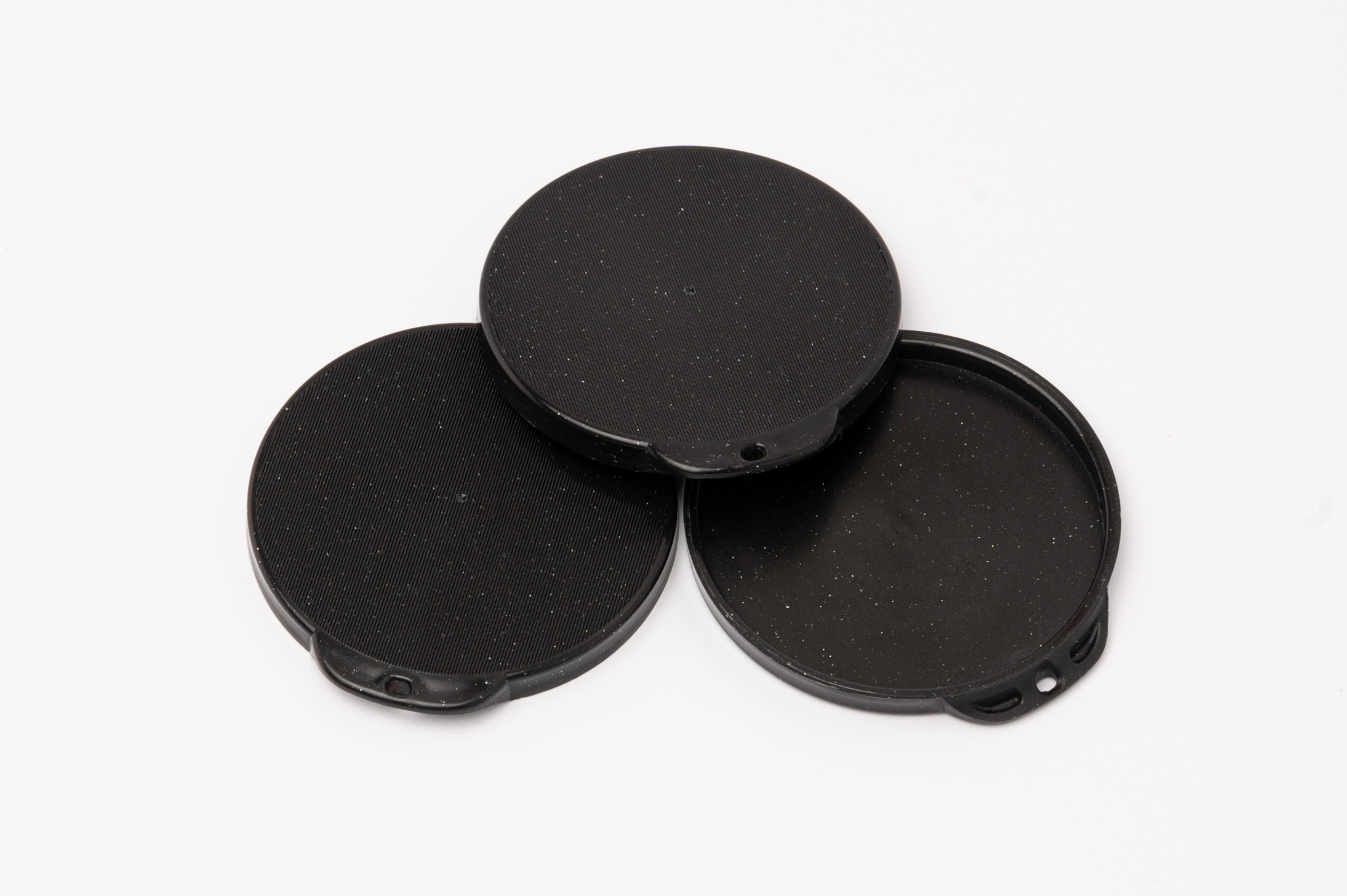 Trzy czarne, okrągłe wieczka z tworzywa sztucznego z drobnymi, białymi plamkami, ułożone warstwowo na białym tle. Wieczka posiadają uchwyty z otworami.