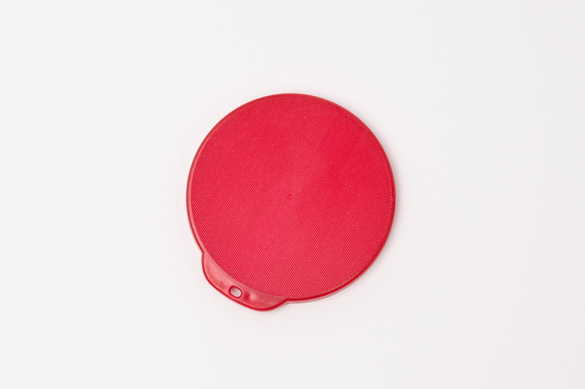 Czerwona, okrągła pokrywka z tworzywa sztucznego z charakterystycznym, prążkowanym wzorem na powierzchni i małym otworem z boku, leżąca na białym tle.