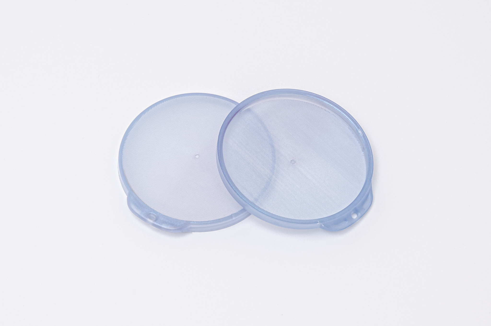 Dwa okrągłe, przezroczyste wieczka z delikatną strukturą wewnątrz, prawdopodobnie do zamykania pojemników z żywnością, leżące na białym tle.