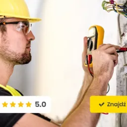 Elektryk w żółtym kasku i kamizelce ochronnej, z profilu, mierzy napięcie w skrzynce rozdzielczej za pomocą multimetru, widoczne przewody i bezpieczniki.