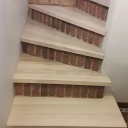 Schody z drewnianymi stopniami i ceglanymi podstopnicami, widok z dołu, ceglana ściana w tle.