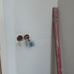 Ściana w trakcie remontu z widocznymi przewodami elektrycznymi wystającymi z dwóch otworów, podłączony nowy przełącznik światła, obok pionowo oparta czerwona poziomica z widocznymi śladami...