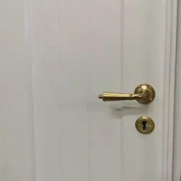 Białe drzwi wewnętrzne z klasyczną, mosiężną klamką i szyldem zamka.