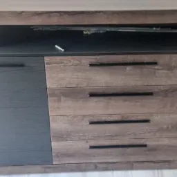 Komoda z szufladami i półkami, w odcieniach brązu i szarości, zamontowana w Tomaszowie Lubelskim. Na blacie komody leżą klucze.