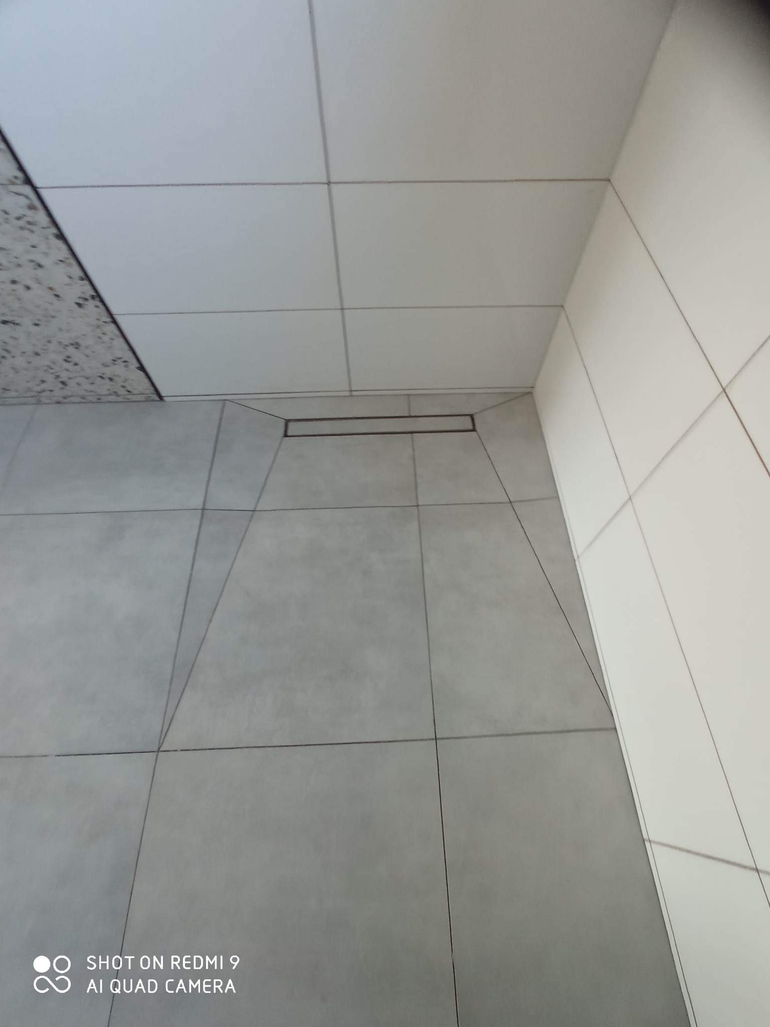 Wykończona łazienka z szarymi płytkami podłogowymi i białymi płytkami ściennymi, widoczny liniowy odpływ podłogowy.