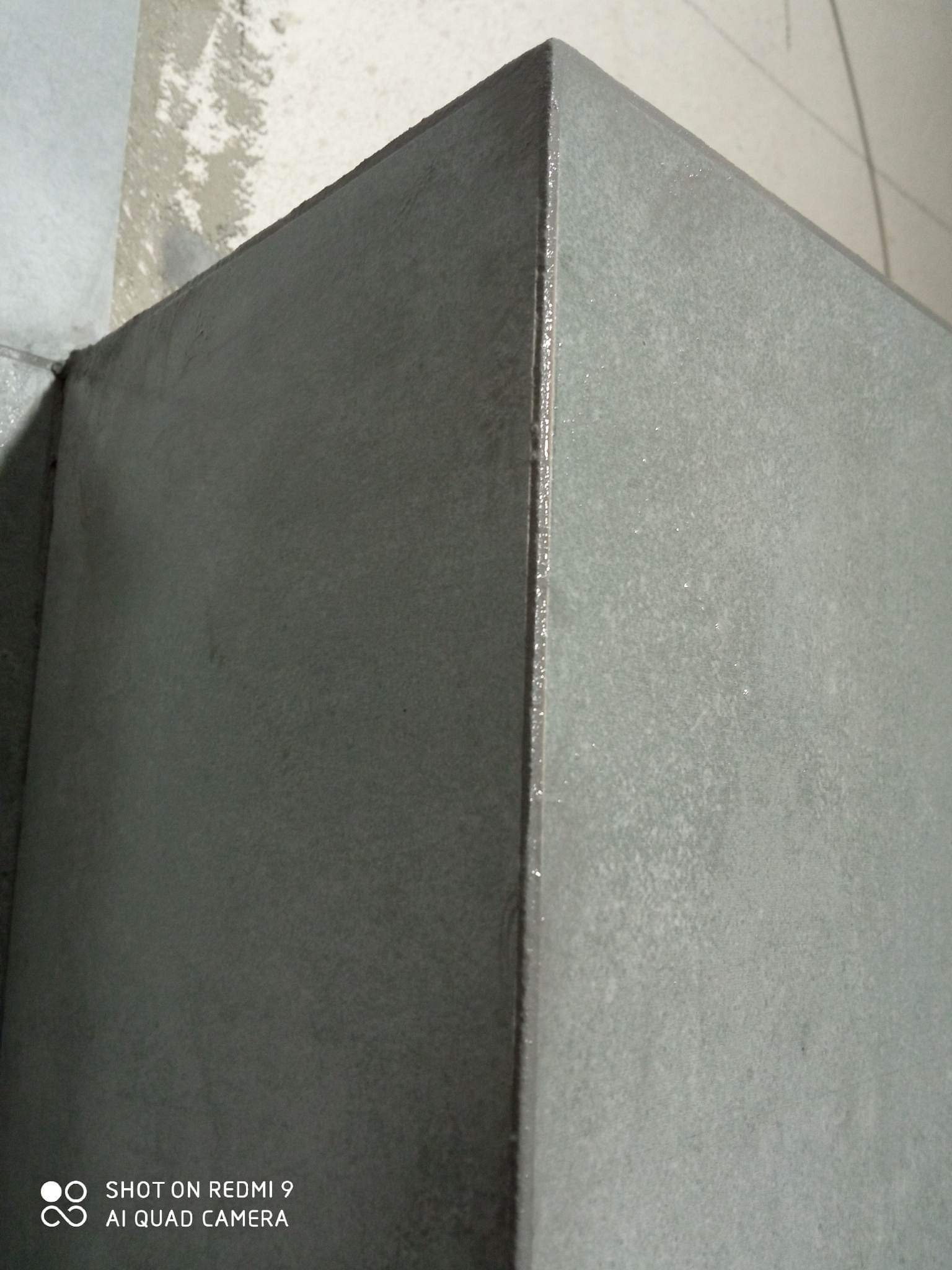 Szary narożnik ściany po świeżo nałożonej gładzi, widoczne niedoskonałości i nierówności powierzchni przed szlifowaniem.