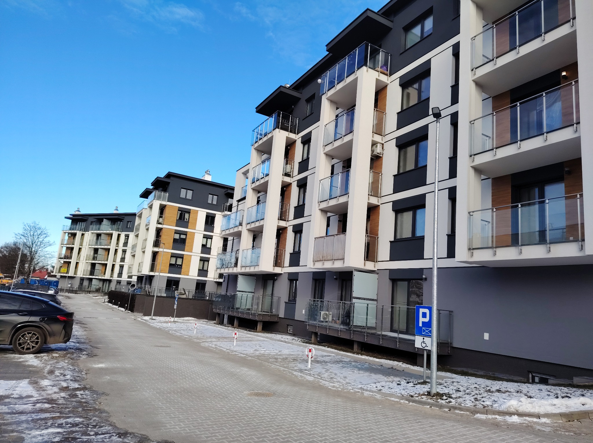 Nowoczesny budynek wielorodzinny z balkonami w Zychorzynie. Elewacja w odcieniach bieli, szarości i czerni. Widoczne szklane balustrady i oświetlenie zewnętrzne.