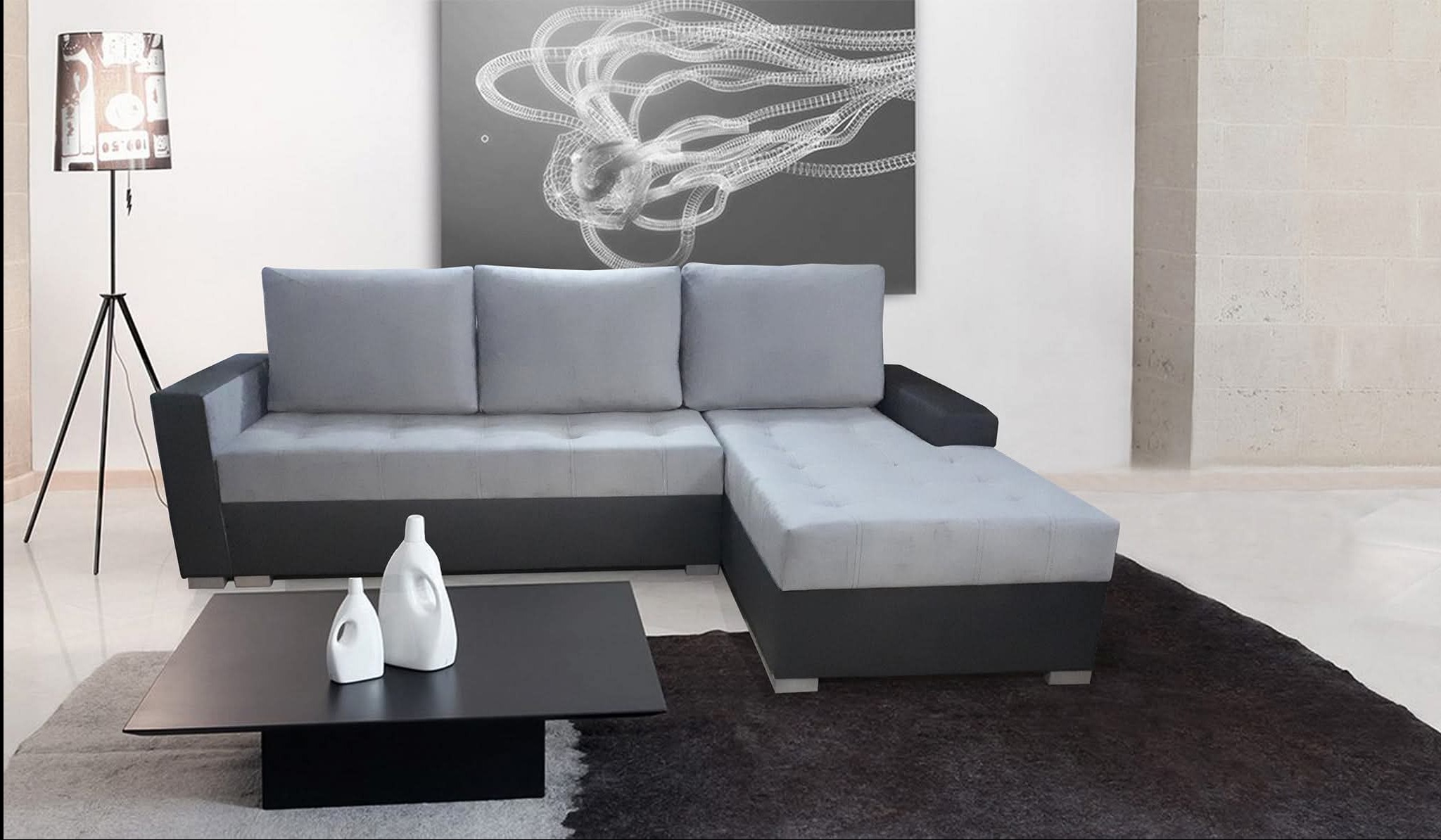 Nowoczesna, narożna sofa w odcieniach szarości z czarnymi akcentami, ustawiona w minimalistycznym salonie z abstrakcyjnym obrazem i lampą na trójnogu.
