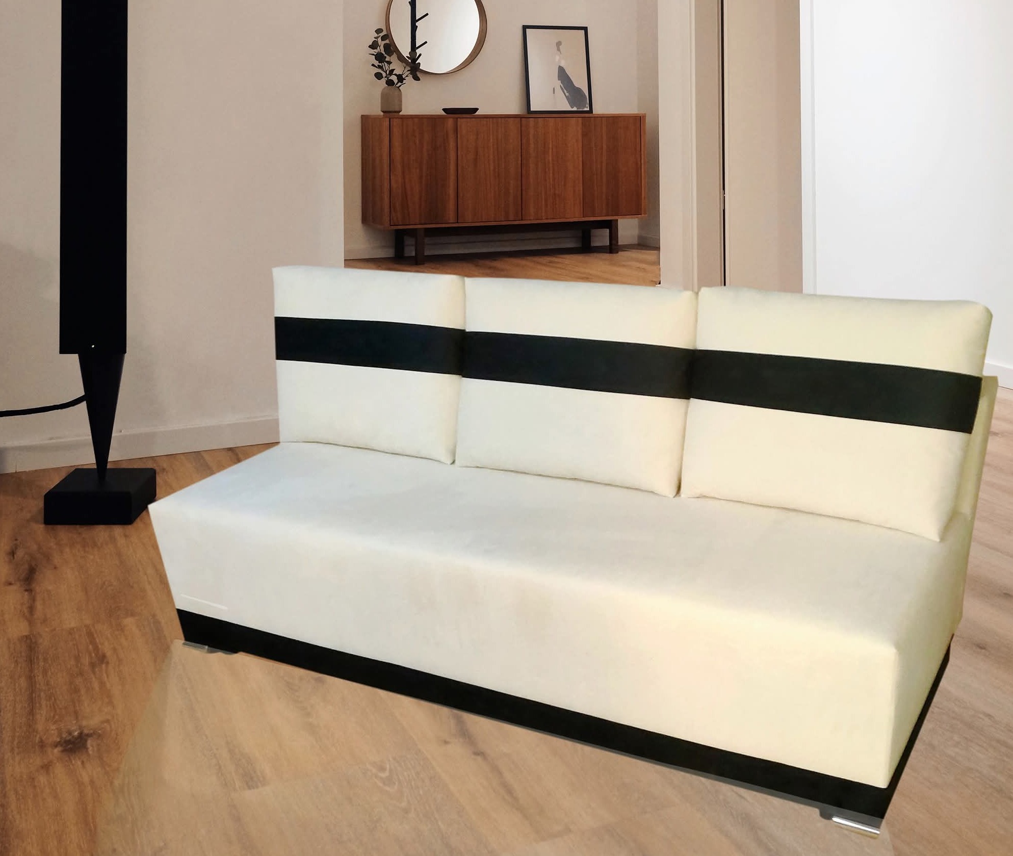 Biała sofa z czarnymi akcentami w nowoczesnym salonie. Widoczny drewniany parkiet, komoda i lampa. Minimalistyczny design.