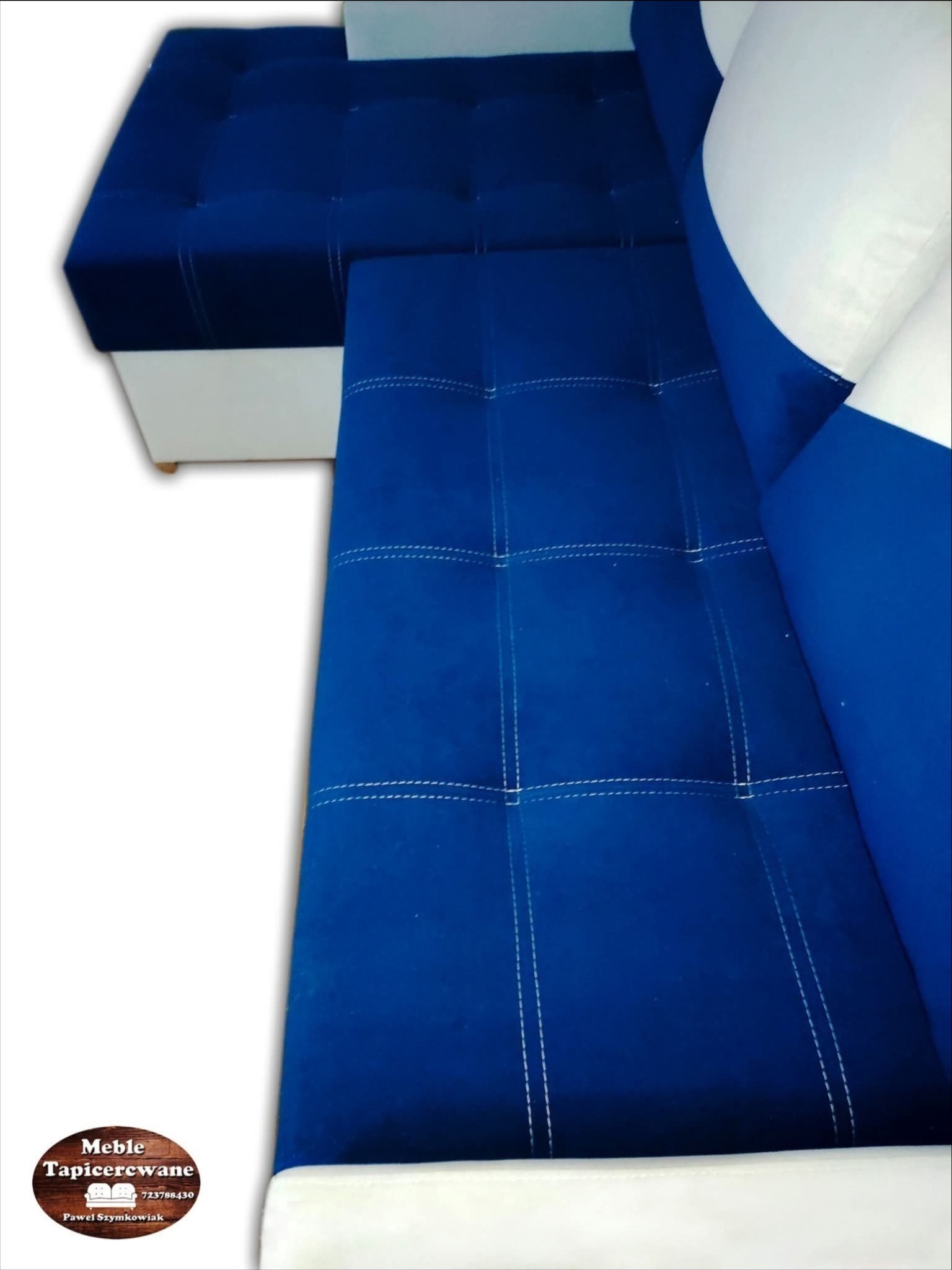 Narożnik tapicerowany w odcieniach błękitu i bieli, z dekoracyjnymi przeszyciami, prezentowany z bliska. Widoczny fragment siedziska i oparcia z poduszkami.