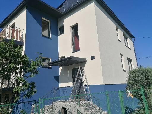 Dwukondygnacyjny dom po remoncie elewacji, z niebieską i białą fasadą, widoczna drabina oparta o wejście.
