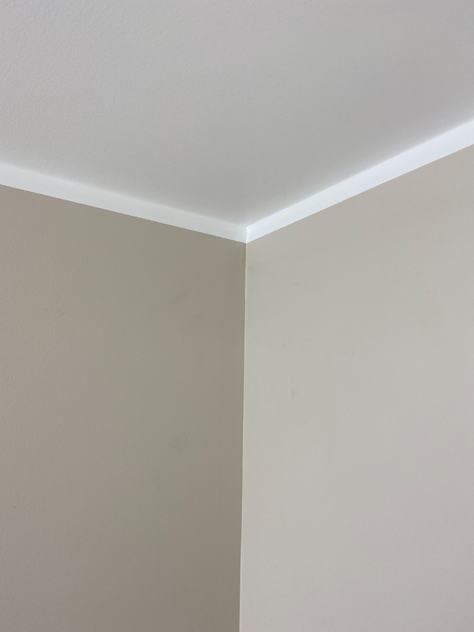 Wnętrze pokoju z pomalowanymi ścianami w odcieniach beżu i szarości, widoczny narożnik ścian i biały sufit z listwą wykończeniową.