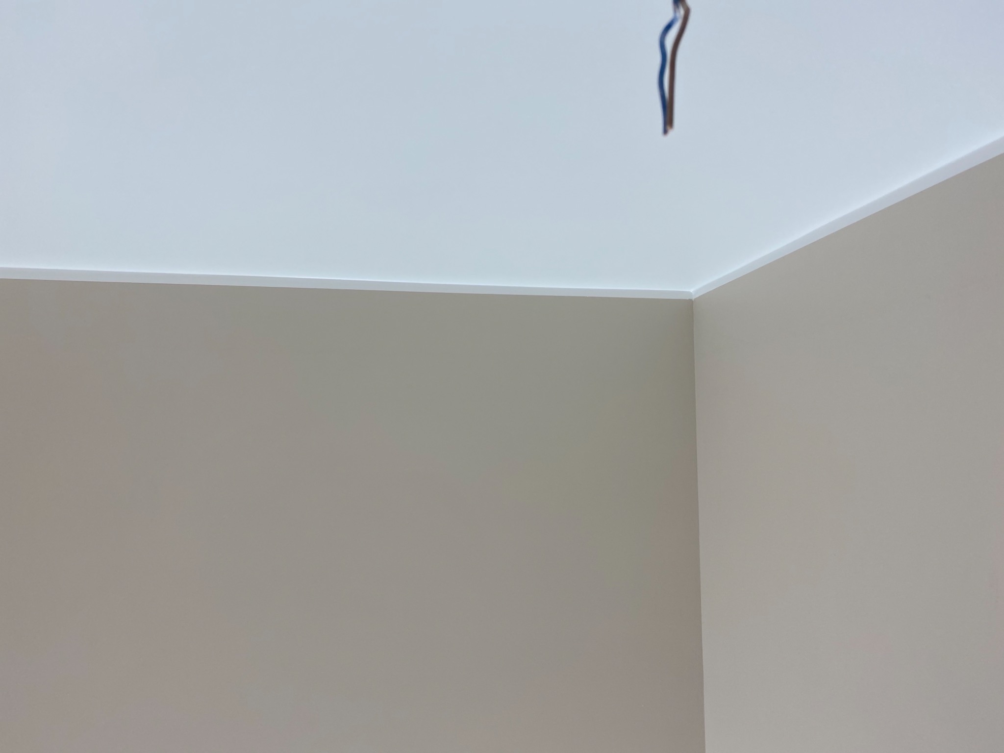 Pomieszczenie po remoncie: gładkie, beżowe ściany, biały sufit z listwą wykończeniową i wystającymi przewodami elektrycznymi.