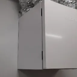 Biała jednostka rekuperacyjna Komfovent zamontowana na ścianie z widocznymi przewodami wentylacyjnymi.