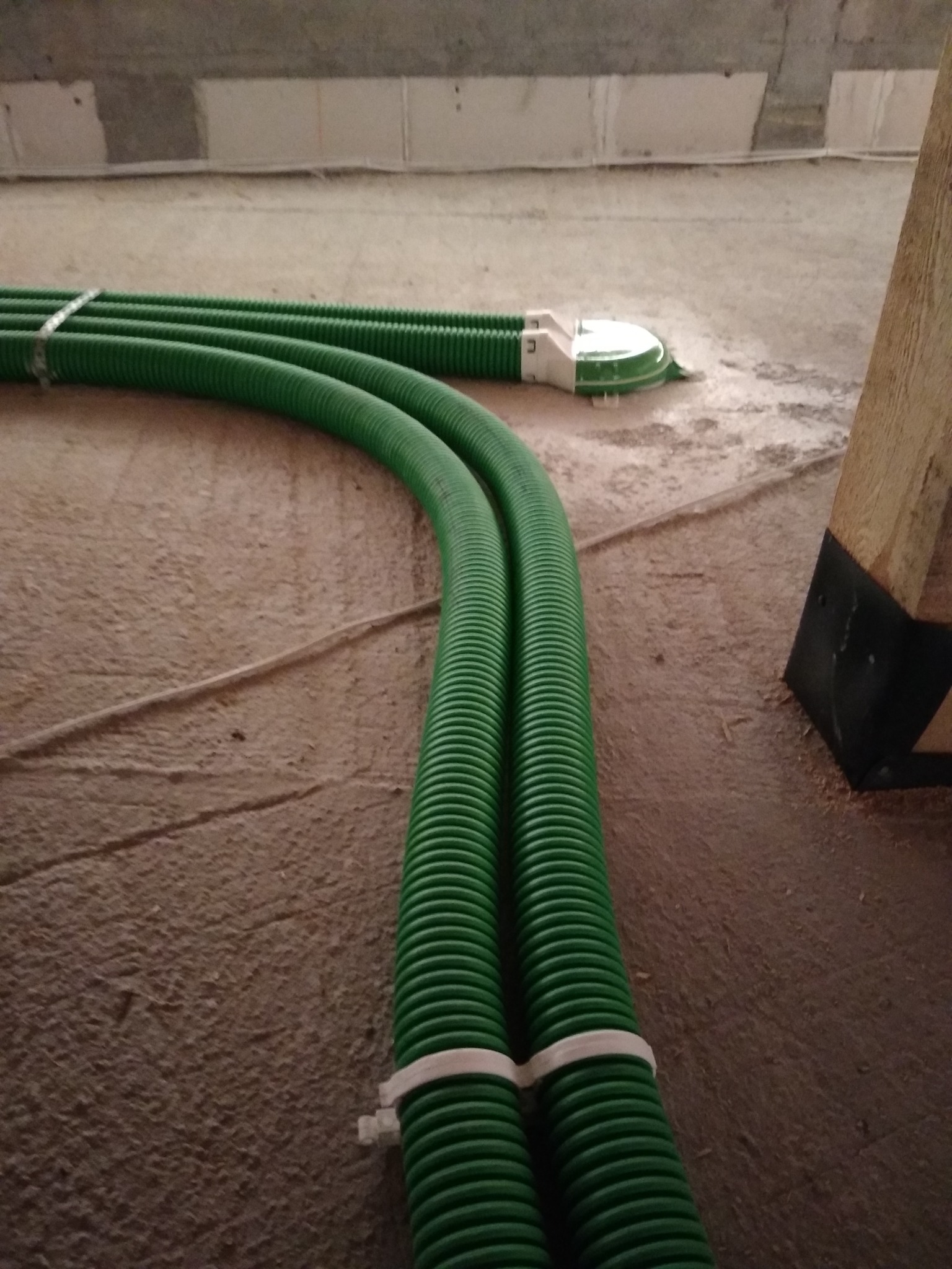 Dwa połączone, zielone, karbowane przewody wentylacyjne leżące na szorstkiej, betonowej podłodze w trakcie instalacji, zabezpieczone białymi opaskami zaciskowymi.