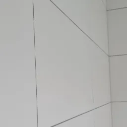 Świeżo położone, duże, białe płytki ceramiczne z szarą fugą na ścianie, widok z dołu na sufit z płyt gipsowo-kartonowych.