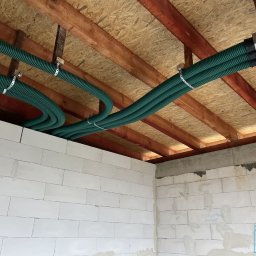 AIR4U - Zielone rury wentylacyjne przymocowane do drewnianego stropu w surowym wnętrzu z białymi ścianami z betonu komórkowego, widoczny fragment instalacji rekuperacji z anemostatem.