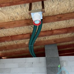 AIR4U - Centrala wentylacyjna z dwoma elastycznymi przewodami wentylacyjnymi, zamontowana pod drewnianym stropem na poddaszu budynku w trakcie budowy.