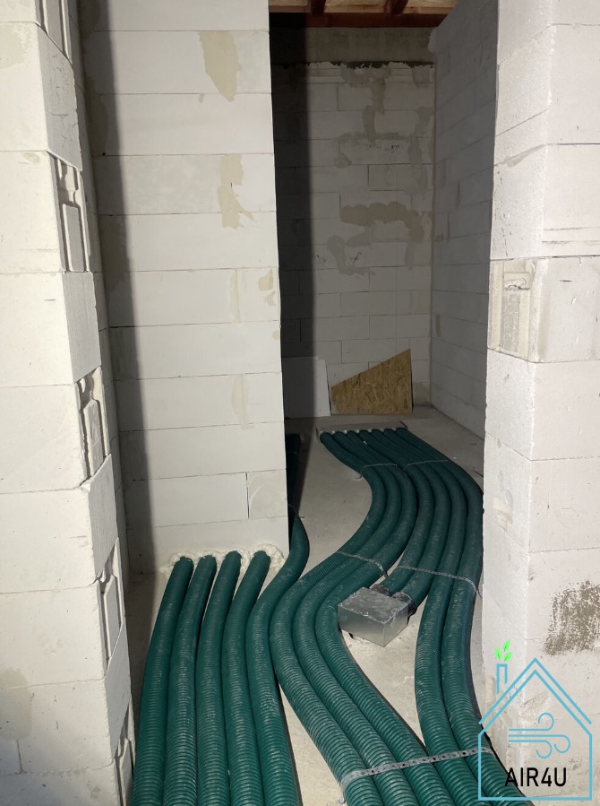 Wnętrze w trakcie montażu systemu wentylacyjnego w Wałczu, widoczne zielone, karbowane rury wentylacyjne prowadzone wzdłuż surowych ścian z bloczków betonowych.