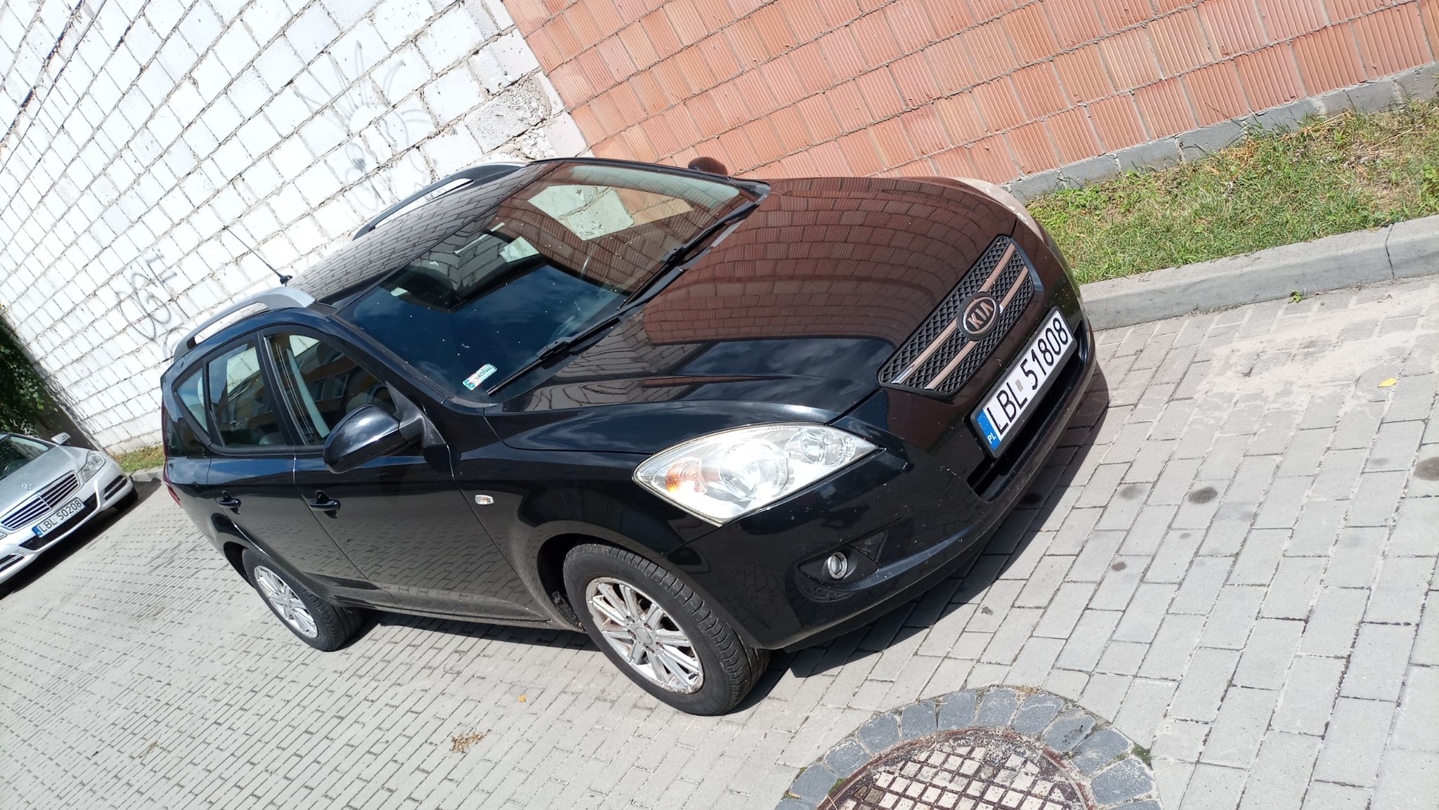 Czarny samochód Kia Ceed kombi zaparkowany na chodniku z kostki brukowej, widoczny z przodu pod kątem, z numerem rejestracyjnym LBL 51808.