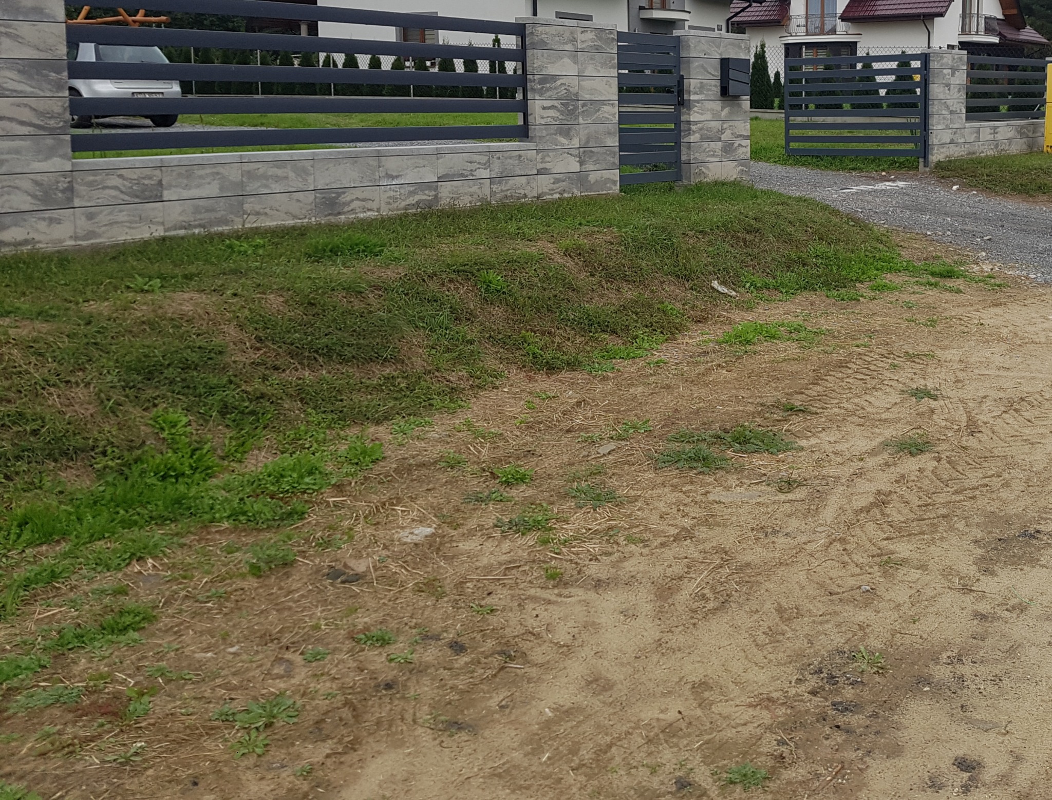 Nowoczesne ogrodzenie panelowe z szarej kostki łupanej i grafitowych przęseł, widok z zewnątrz posesji na tle domów.