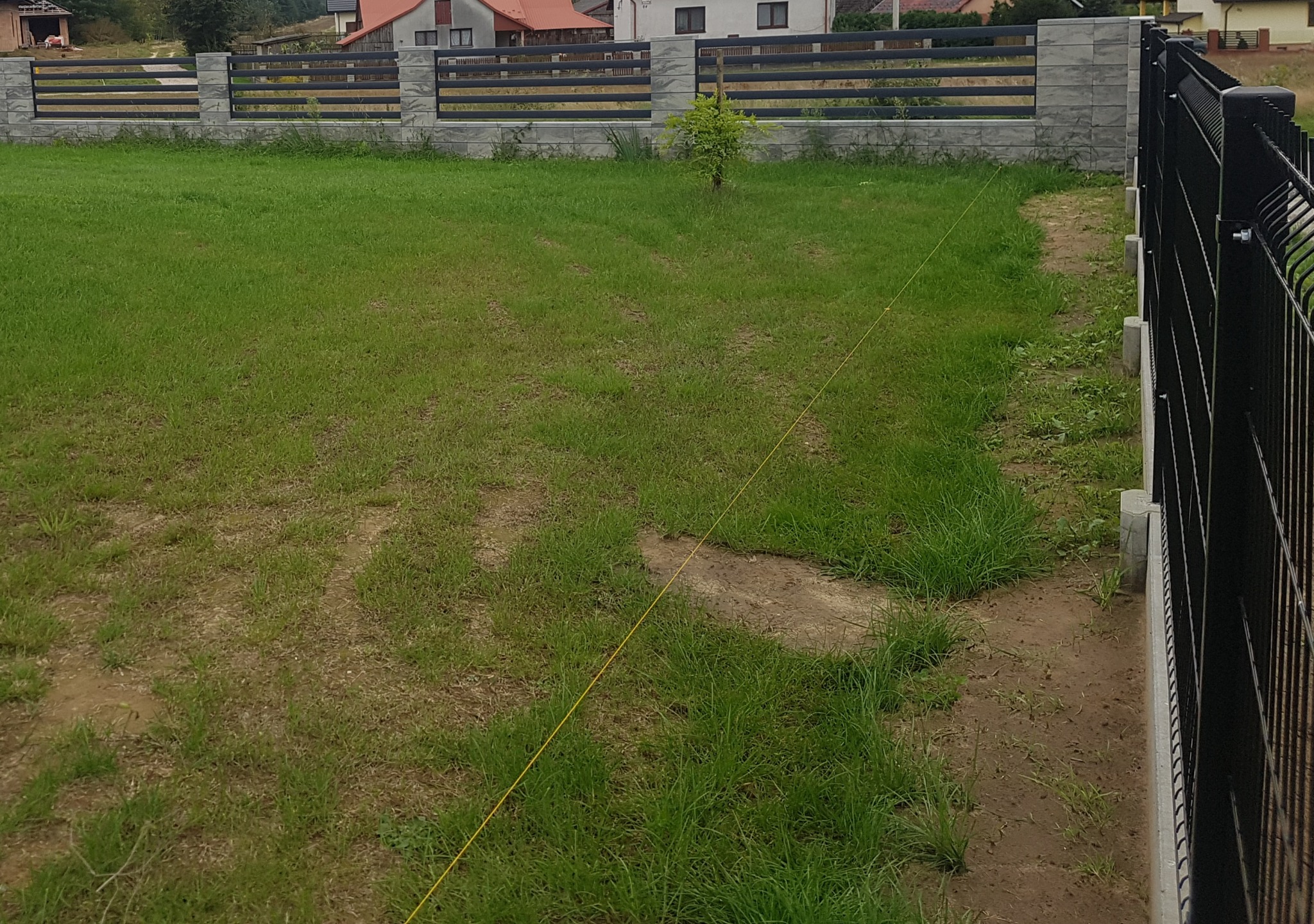 Montaż nowoczesnego ogrodzenia panelowego w Dąbrowie Tarnowskiej, widoczna wytyczona linia pod fundament, trawa z widocznymi śladami prac ziemnych.