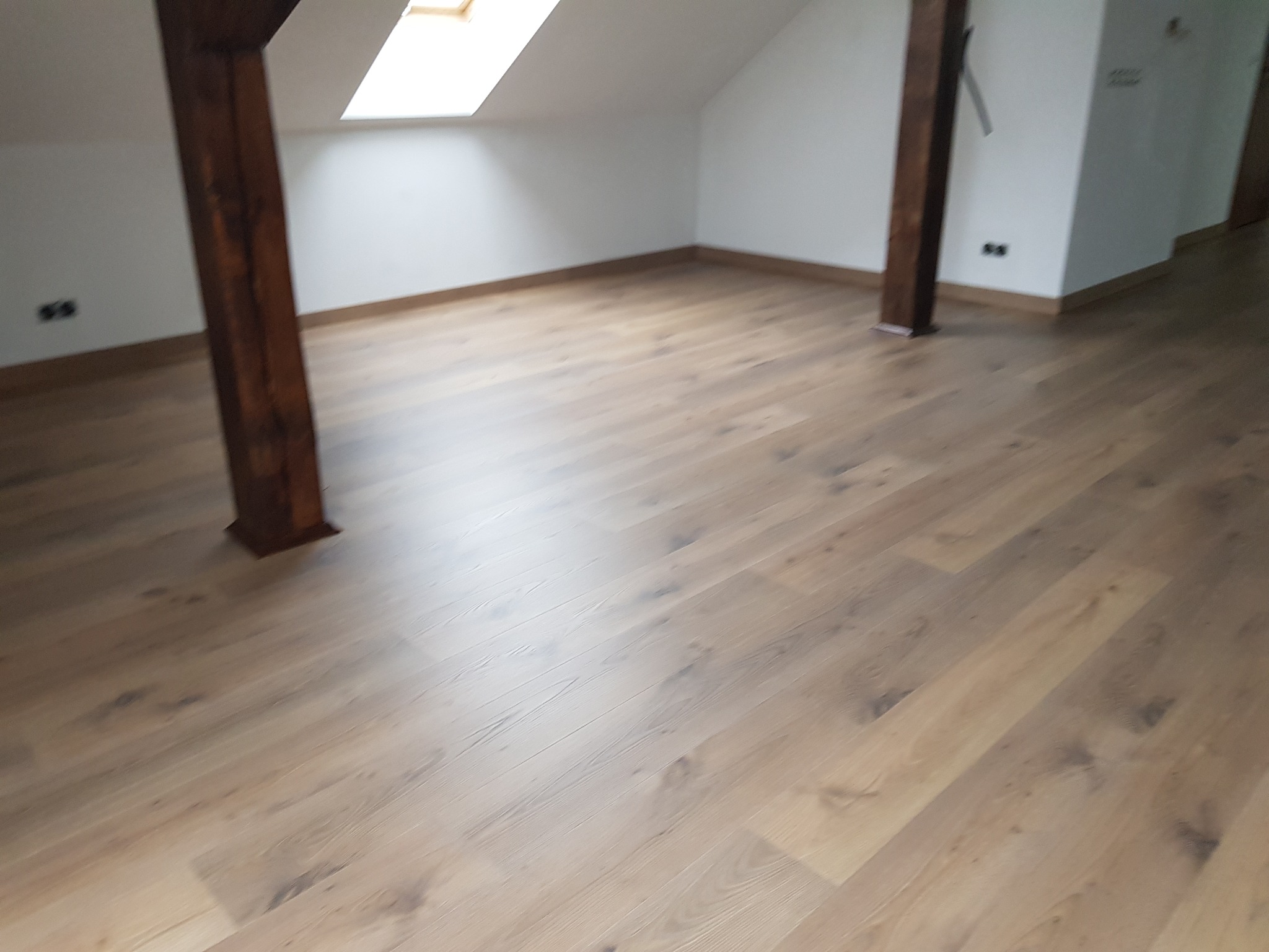 Jasne panele podłogowe w nowym poddaszowym pokoju z drewnianymi belkami i oknem dachowym.