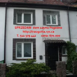 Dwupiętrowy dom w zabudowie szeregowej z ceglaną obudową okien, ciemną stolarką i niewielkim ogródkiem z niskim żywopłotem oraz bramką z ozdobnymi elementami.