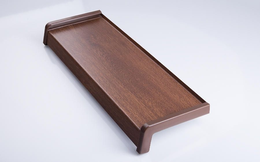 Brązowy parapet z tworzywa sztucznego imitującego drewno, widoczny z boku pod kątem, na jasnym tle.