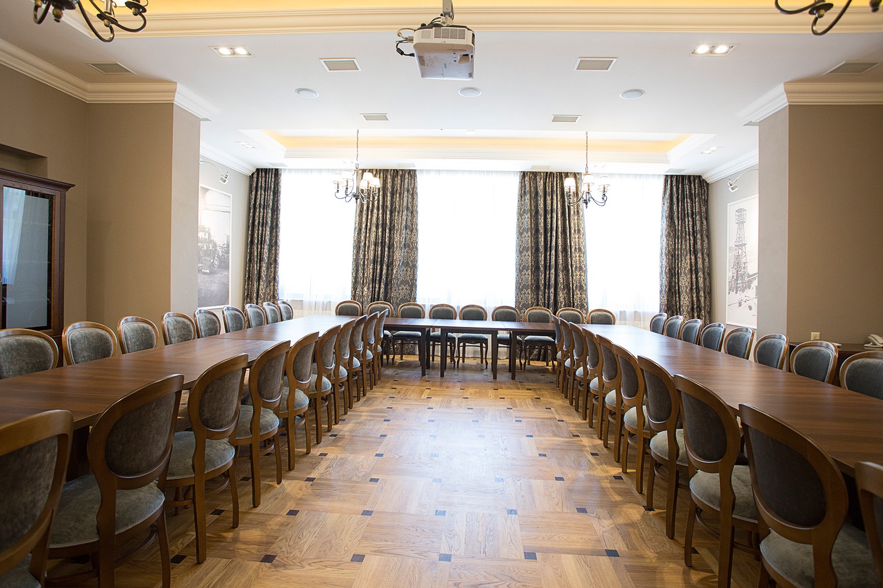 Sala konferencyjna w hotelu Pałac Polanka z długim stołem, krzesłami, projektorem sufitowym, oświetleniem i dekoracyjnymi zasłonami.