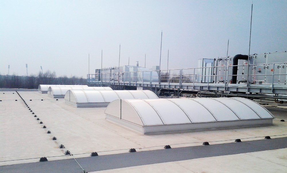 System odgromowy na dachu płaskim budynku przemysłowego z świetlikami kopułowymi, widoczne zwody pionowe i przewody odprowadzające mocowane do dachu za pomocą uchwytów.