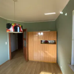 Pokój z odnowioną podłogą panelową, pomalowanymi na zielono ścianami, otwartymi drzwiami i szafą z lat 70-tych z widoczną dekoracją w otwartej wnęce.