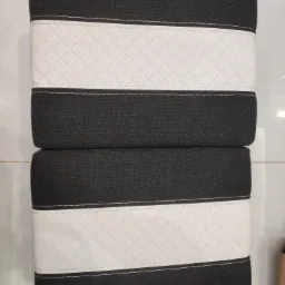 Dwa czarno-białe materace ułożone jeden na drugim, z białym pasem w romby pośrodku i ciemną tkaniną na górze i dole.