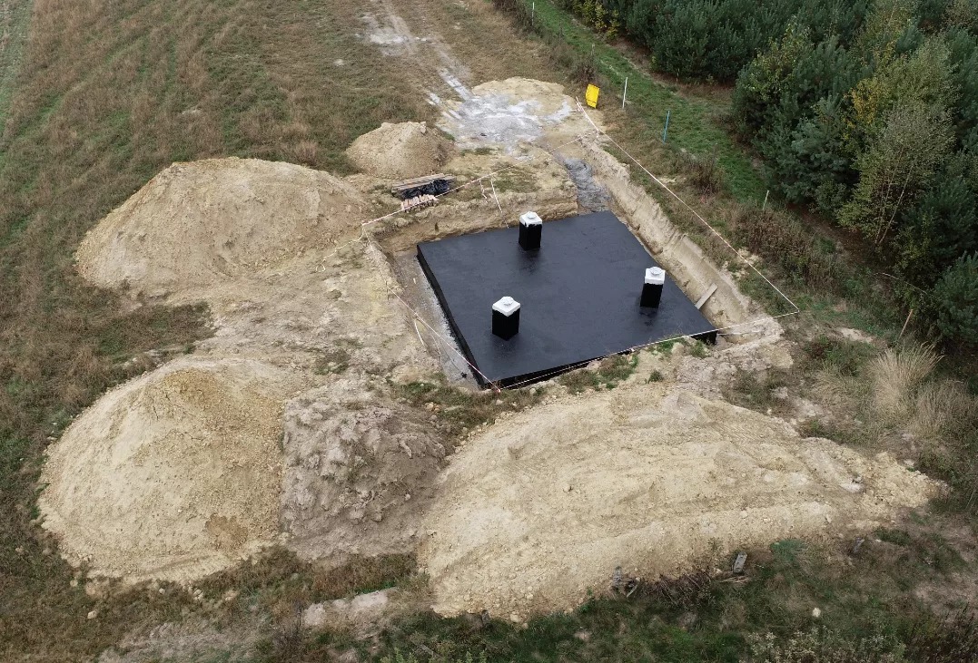 Fundament płyty z izolacją, widok z góry. Wokół wykopu hałdy ziemi, w tle las. Etap budowy domu jednorodzinnego, teren przygotowany pod wylanie betonu.