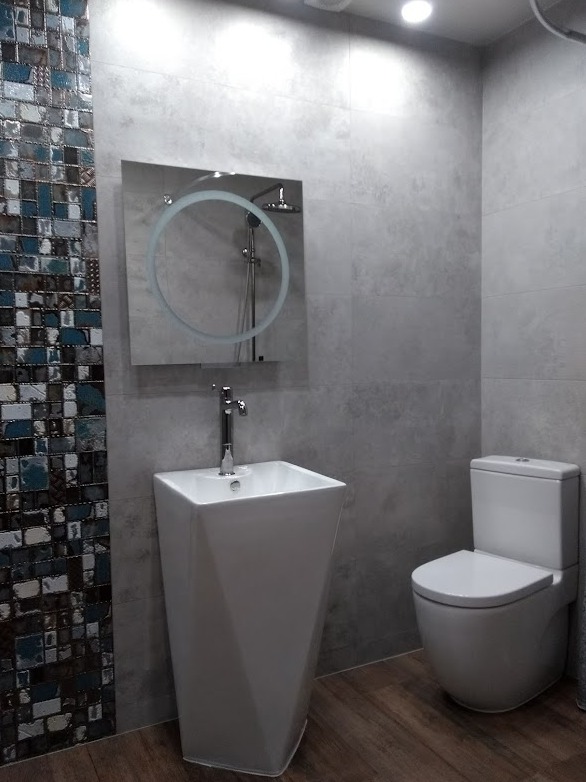 Nowoczesna łazienka z kwadratową umywalką wolnostojącą, podświetlanym lustrem i mozaiką na ścianie, drewnopodobne płytki na podłodze.