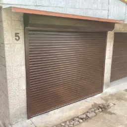 Zewnętrzna brama rolowana w kolorze brązowym, zamontowana w garażu z numerem '5' na ścianie, widok z zewnątrz.