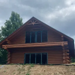 Dom z bali w stylu góralskim z ciemnozielonymi oknami, położony na wzniesieniu, widoczne materiały budowlane.