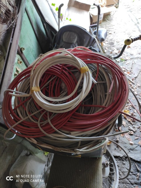 Splot czerwonych, białych i szarych przewodów elektrycznych, owiniętych żółtą taśmą, ułożony na starym wózku transportowym w zabałaganionym otoczeniu.