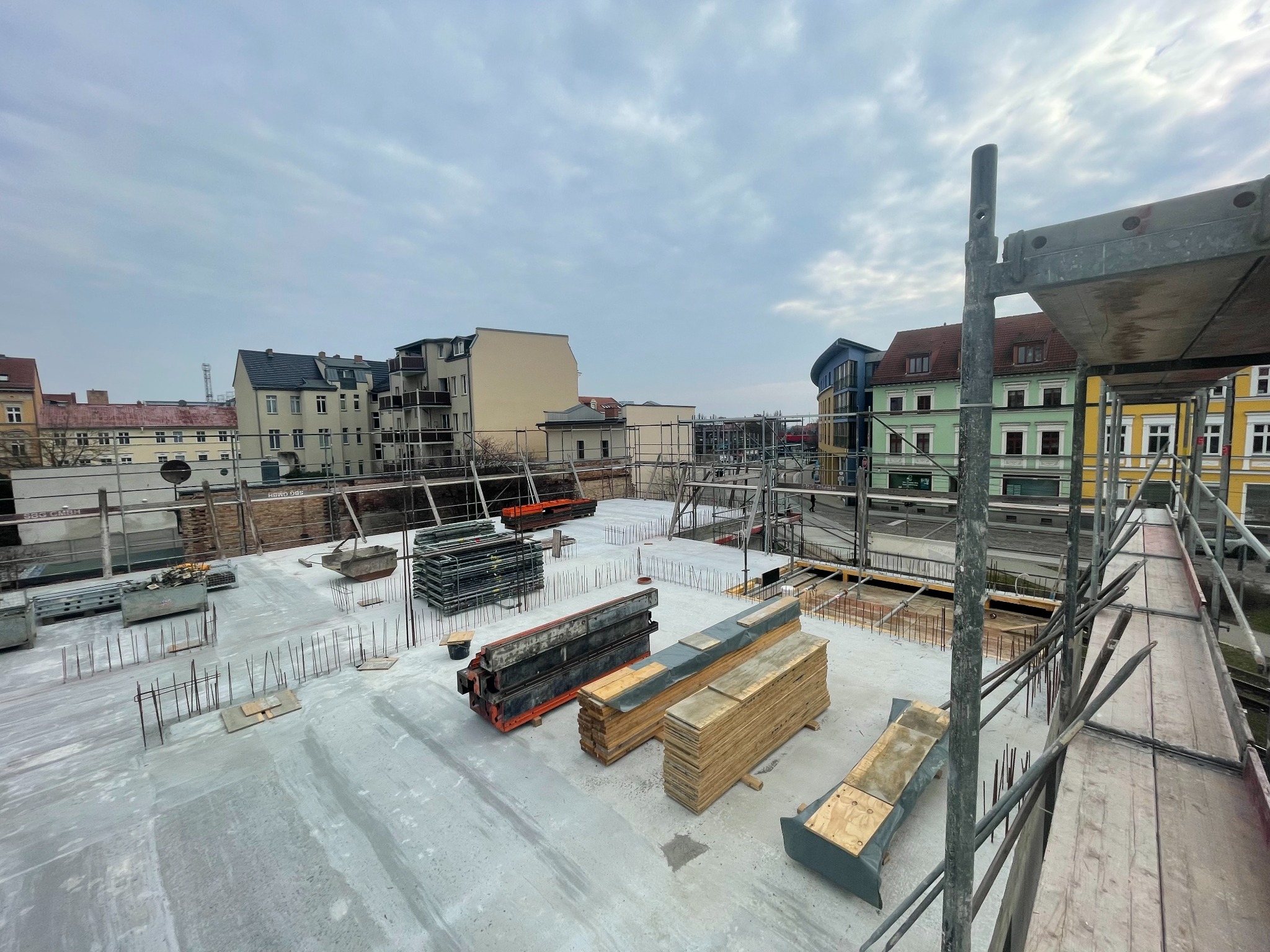 Betonowa płyta stropowa w trakcie budowy, widoczne szalunki, zbrojenia i rusztowania na tle zabudowy miejskiej pod pochmurnym niebem.